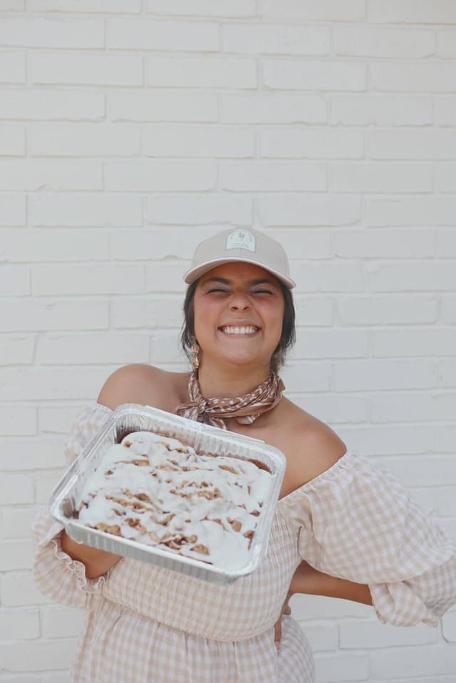Ellie beaming, holding a pan of iced cinnamon rolls
